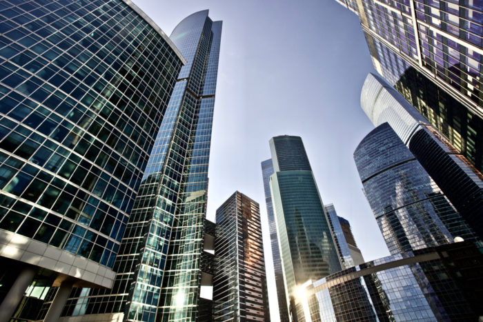 looking up at several tall glass and metal buildings